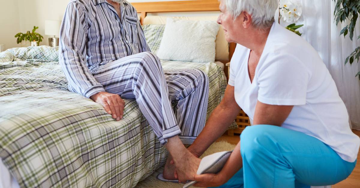5 Nejlepších bačkor pro seniory: Pohodlná a bezpečná obuv pro každodenní nošení 1 an elderly person sitting on a bed while a healthcare professional examines their foot, focusing on comfortable and supportive footwear like zdravotní bačkory.