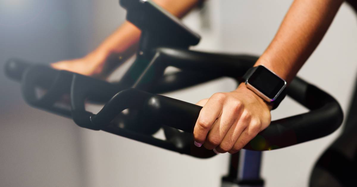 5 Nejlepších rotopedů pro seniory: Cvičte pohodlně a bezpečně v pohodlí domova 1 a person using a recumbent exercise bike, gripping handles while wearing a smartwatch for fitness tracking