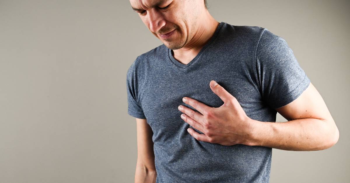 a person clutching their chest, indicating potential chest pain or discomfort related to cardiovascular health concerns