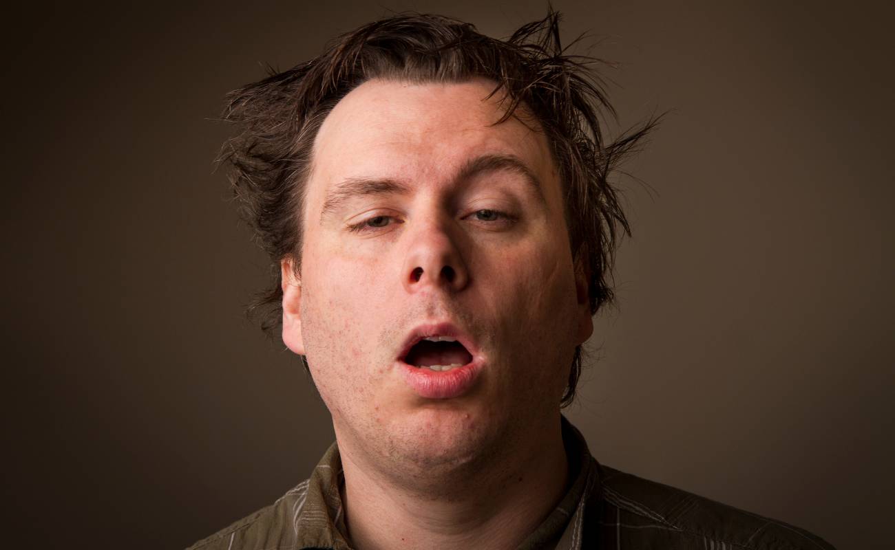 a person singing or vocalizing with an open mouth against a neutral background, showing signs of effort or expression.